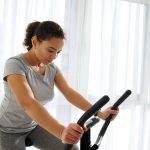 Attractive fit woman exercising on a stationary bike at home on a beautiful sunny day. Cardio workout.